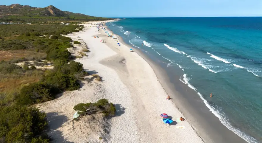 L'oasi di Bidderosa, una spiaggia sarda con sabbia chiara, vegetazione mediterranea e mare turchese, accoglie bagnanti sotto ombrelloni colorati.