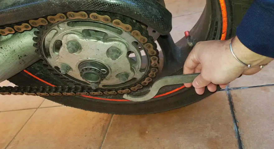 Mano con chiave inglese che lavora sulla catena di una moto, mostrando come tirare la catena della moto per la manutenzione.