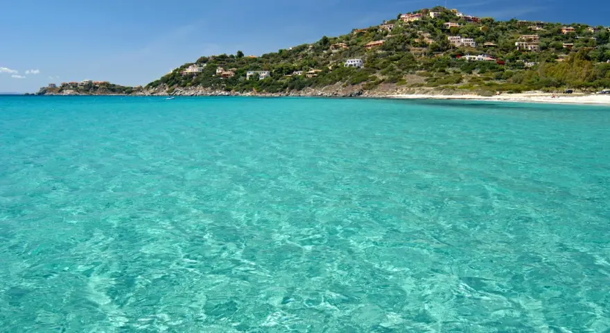 Acque cristalline e una collina verdeggiante punteggiata di case bianche e rosse, con la **spiaggia Torre delle Stelle** che si estende in lontananza.
