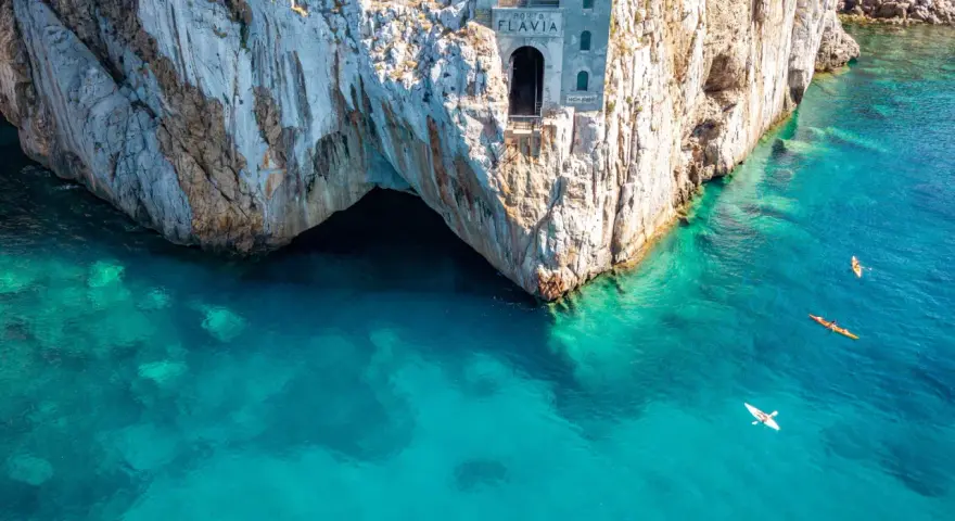 Porto Flavia, un'antica struttura legata alle miniere abbandonate della Sardegna, si affaccia su un mare cristallino. Kayak solcano le acque turchesi.