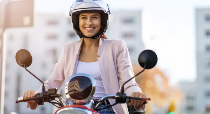 Donna sorridente in motorino, con casco bianco, rispetta l'obbligo casco motorino per la sua sicurezza.