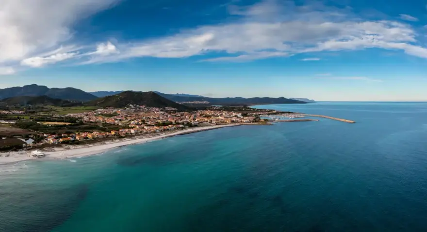 Vista aerea di Posada, Siniscola, con la sua spiaggia dorata, il mare turchese e le case colorate che si affacciano sulla costa.