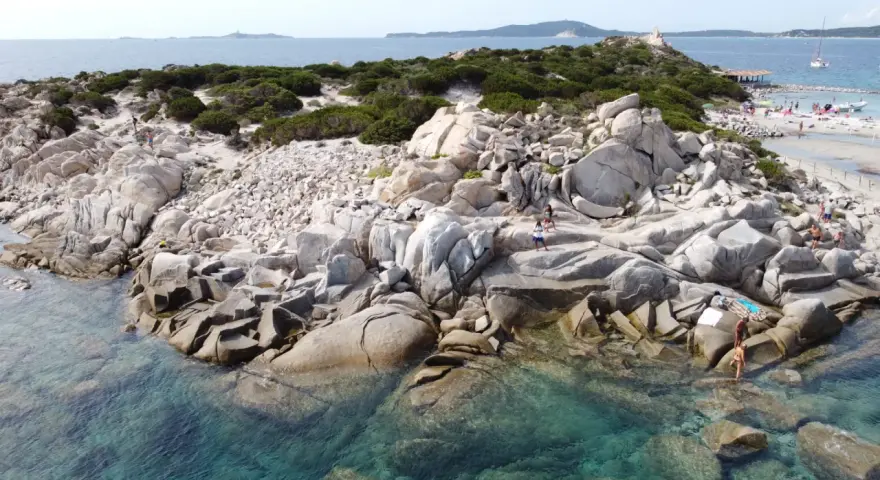 Scogliere rocciose e acque cristalline sulle spiagge a Villasimius. Turisti esplorano la costa selvaggia e si godono il sole.