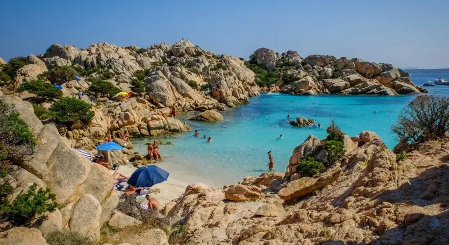 Una baia con rocce granitiche scolpite dal vento e acque turchesi cristalline, tra le spiagge più belle sardegna nord. Gente rilassata sotto gli ombrelloni.