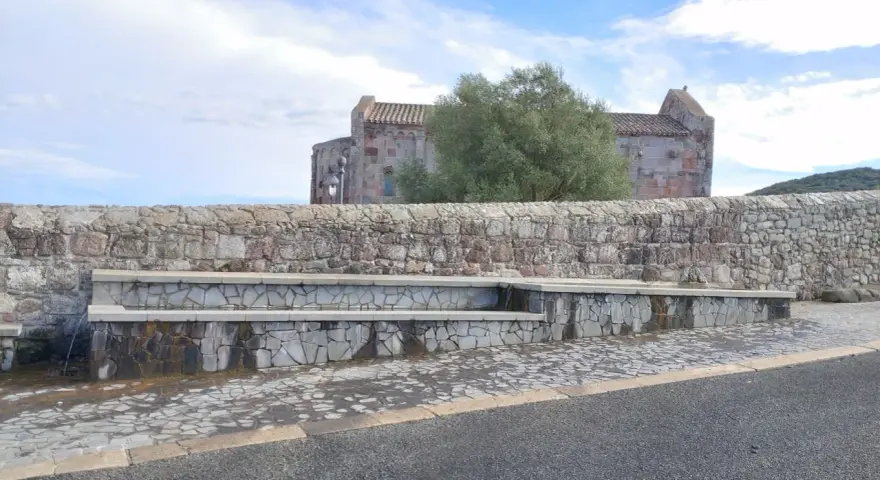 Fontana in pietra con scorci di un antico edificio religioso, un'oasi di pace ad **Allai, Sardegna**.