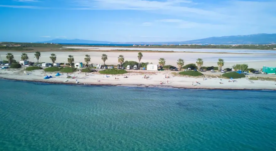 Spiaggia di Putzu Idu con palme, camper e gente che si gode il sole. Acqua cristallina e cielo azzurro.