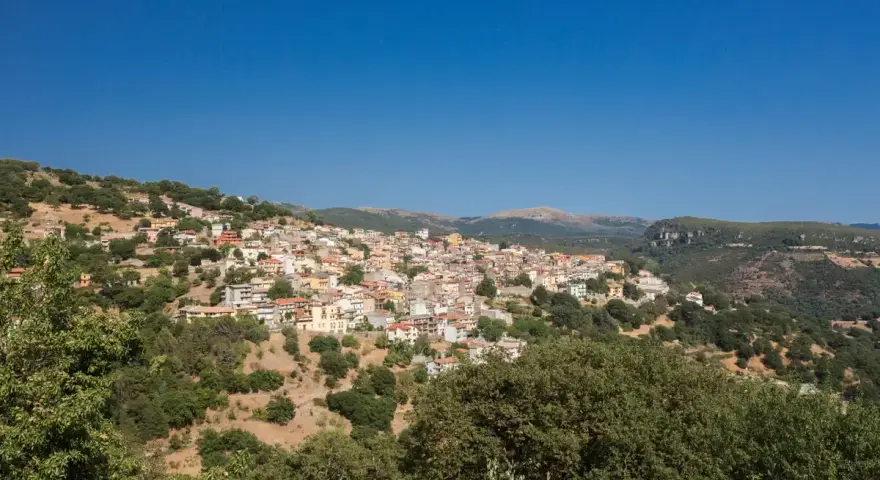 Panoramica di Seulo, Sardegna, con case colorate arroccate su una collina verdeggiante sotto un cielo azzurro.