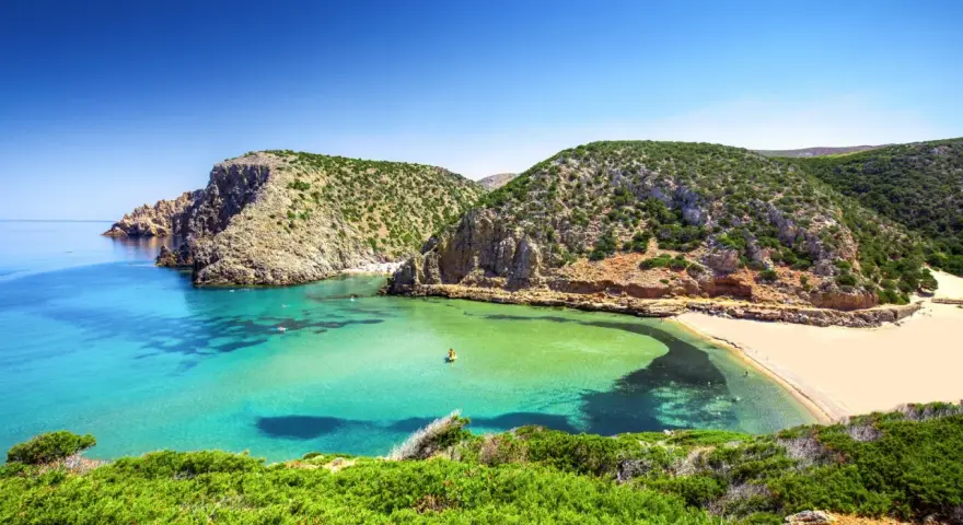 Baia con acque cristalline e sabbia dorata, incastonata tra scogliere verdi. Un vero gioiello tra le spiagge più belle in Sardegna.