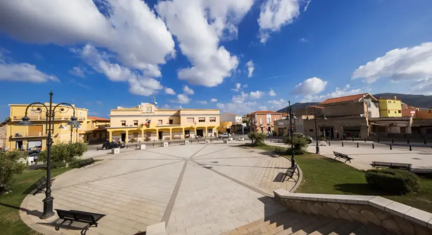 Piazza di San Giovanni Suergiu con edifici gialli e cielo azzurro.