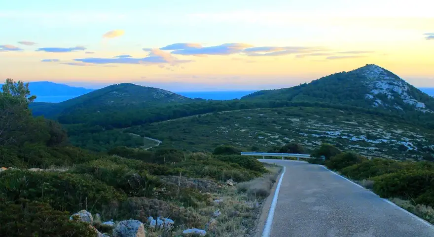 Strada panoramica verso il monte Doglia al tramonto, con colline verdi e cielo colorato.