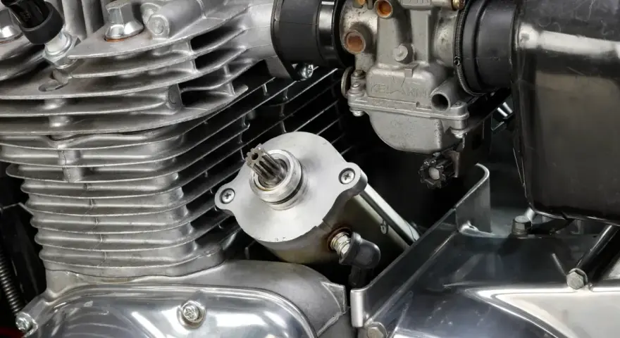 Dettaglio del motore di una moto: il test del motorino di avviamento è in primo piano, con il carburatore e le alette di raffreddamento visibili.