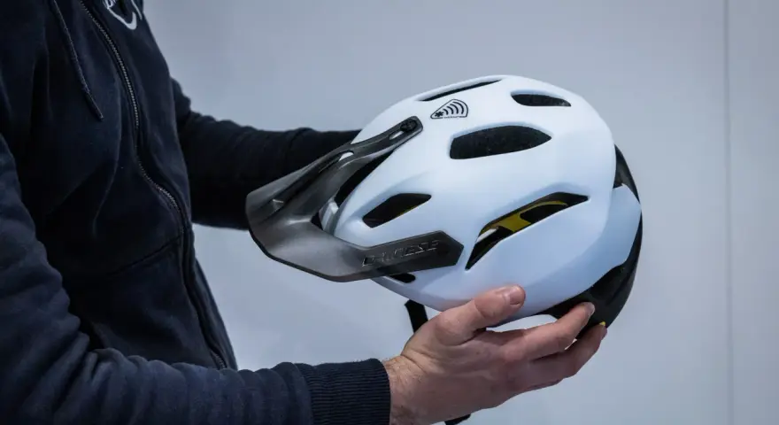 Mani che tengono la calotta esterna di un casco da bici bianco con visiera scura e logo Dainese.