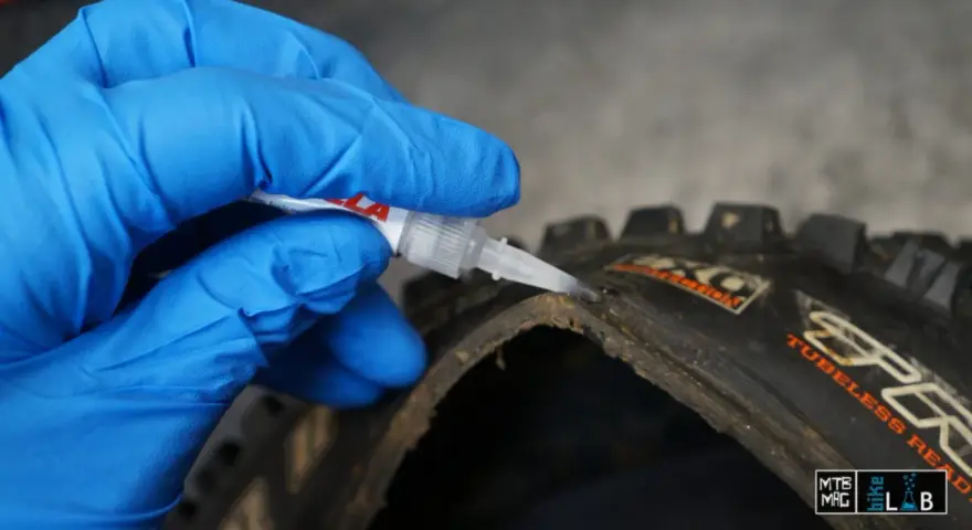 Mano con guanto blu applica colla per pneumatici tubeless riparazione su un copertone da MTB.