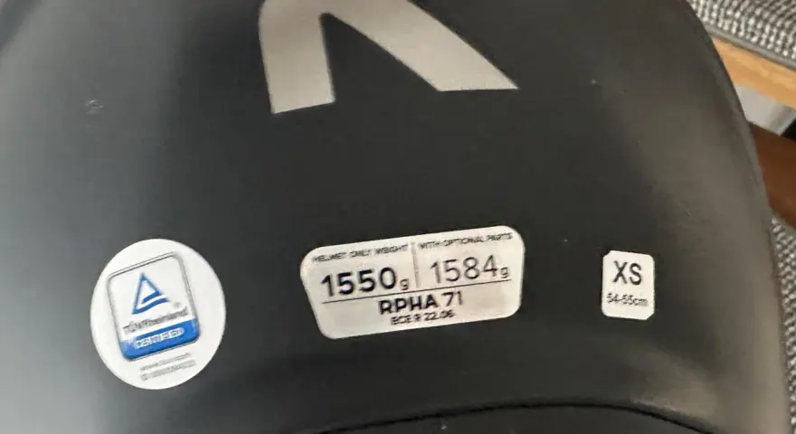 Casco nero con logo R argentato. Etichette indicano peso, modello RPHA 71, certificazione e taglia XS. Sul casco possono essere applicati adesivi.
