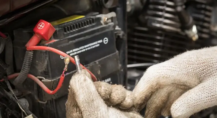 Mani guantate lavorano sulla batteria 12V della moto, forse per il tempo di ricarica.