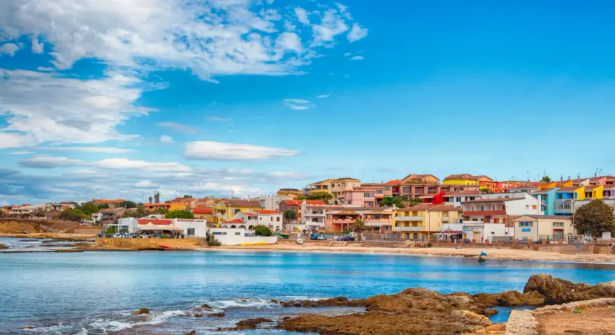 Colorate case affacciate sul mare blu, con rocce in primo piano. Il centro storico di Porto Torres, un incanto sardo.