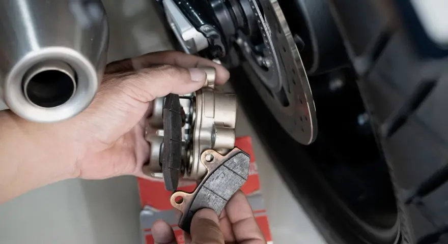 Mani che sostituiscono pastiglie cristallizzate su una moto. Si vede la pinza del freno e il disco.