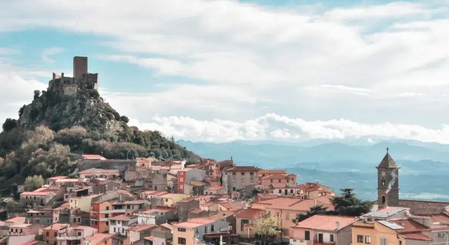 Borgo medievale di Burgos, Sardegna, con castello in rovina su uno sperone roccioso e case colorate a valle.