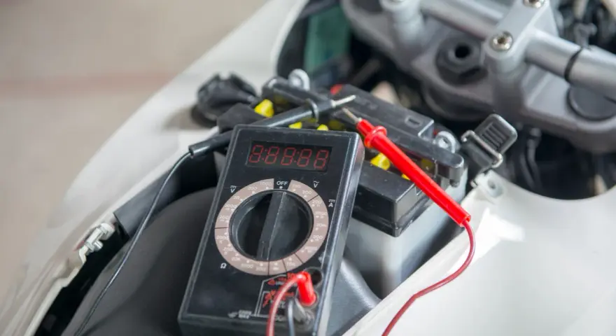Multimetro collegato alla batteria della moto per verificarne lo stato prima di staccare la batteria moto inverno.