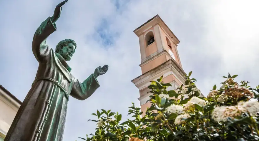 Statua di San Francesco con campanile e fiori. Il **Nuoro significato** di questo luogo è legato alla spiritualità e alla natura.
