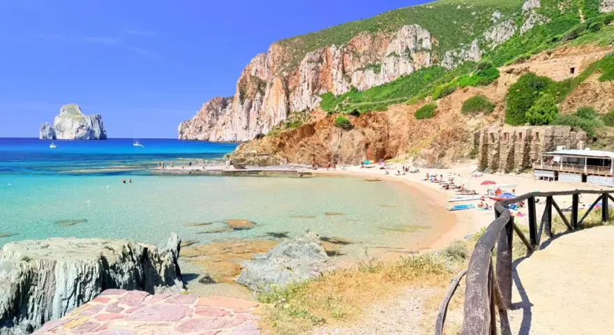 Spiaggia di Masua con acque cristalline, scogliere imponenti e il Pan di Zucchero all'orizzonte. Relax e natura incontaminata.