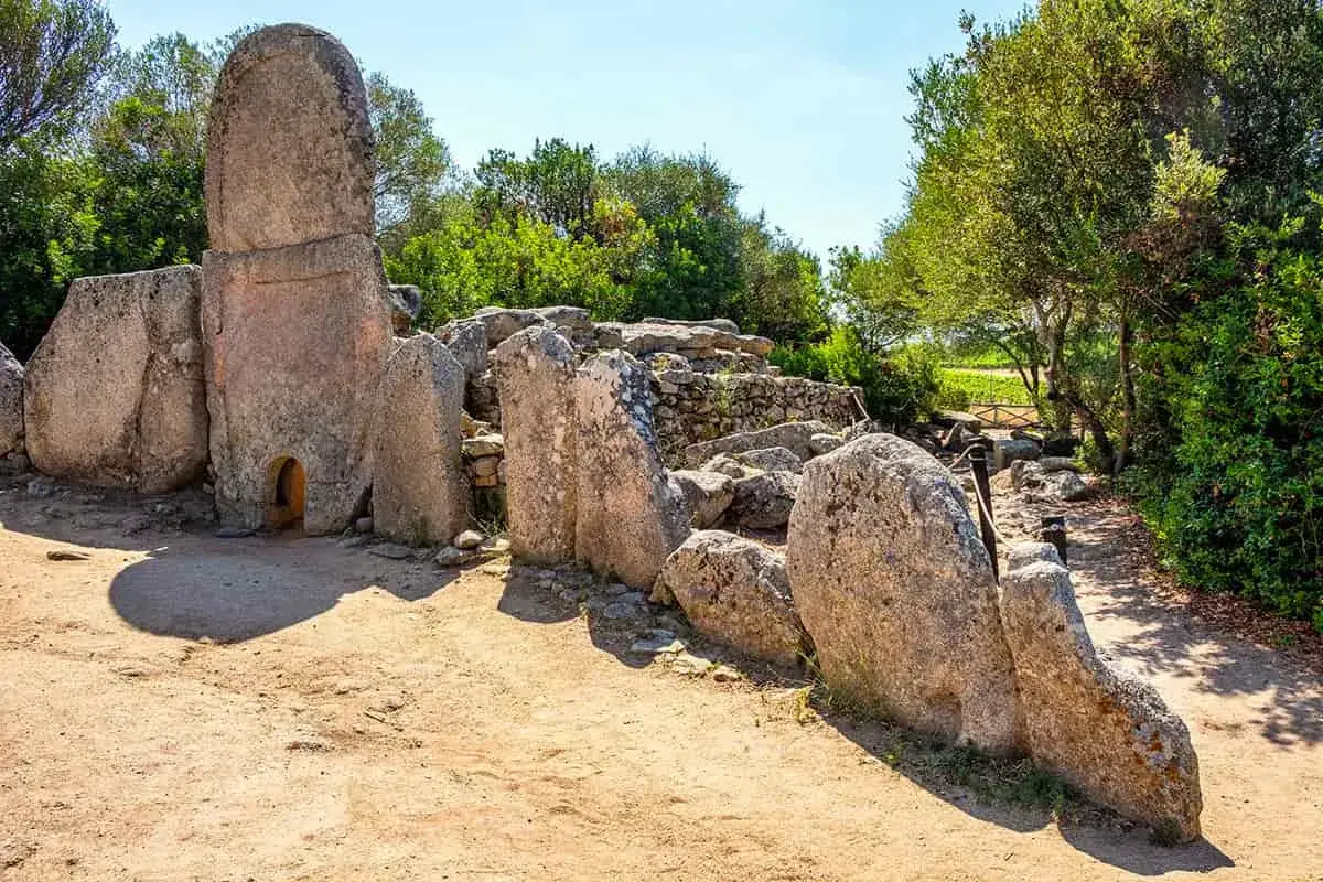 Antica tomba dei giganti in Sardegna, con imponenti pietre erette e un ingresso ad arco, immersa nel verde.
