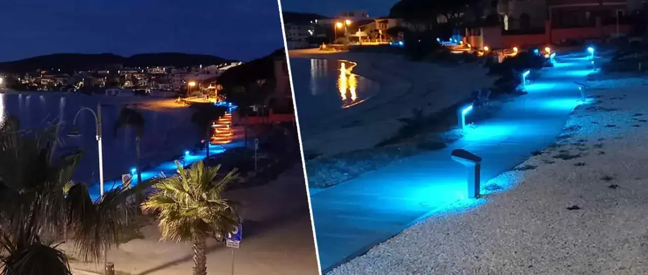 Passeggiata illuminata da luci blu sul lungomare di Golfo Aranci sera. Riflessi sull'acqua e palme.