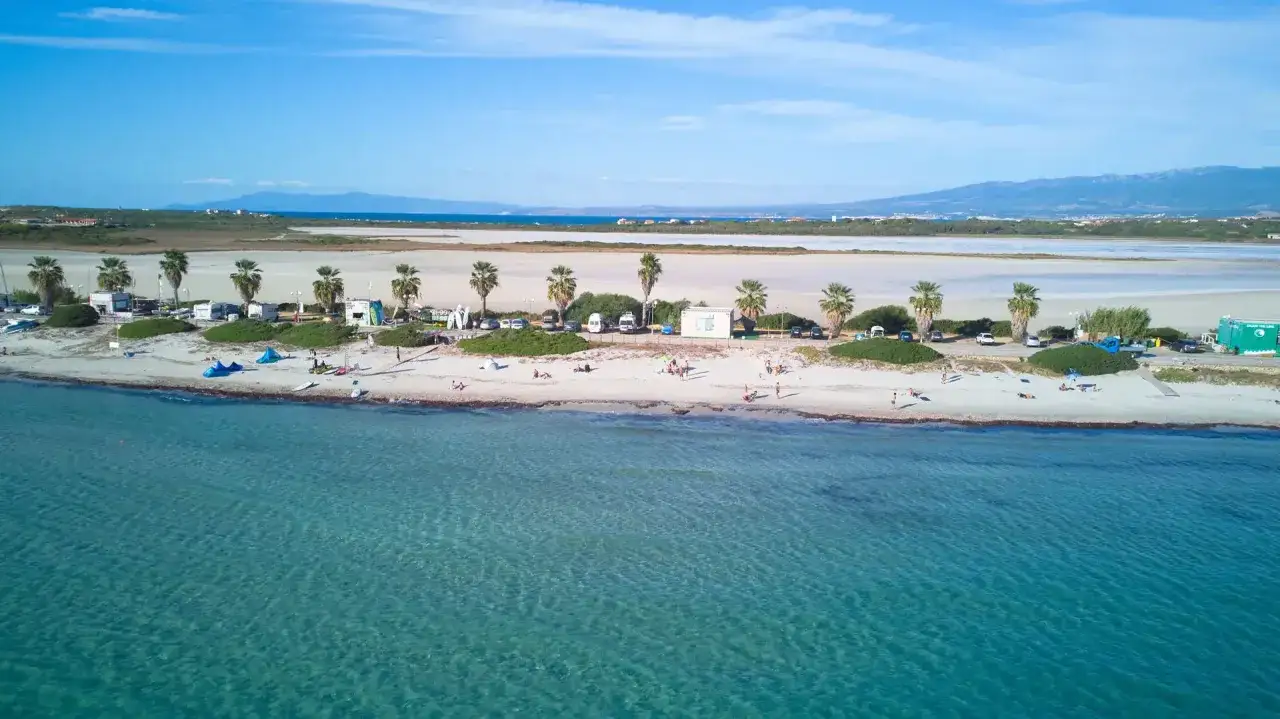 Spiaggia di Putzu Idu con palme, camper e persone che si godono il sole. Acqua cristallina e cielo azzurro.