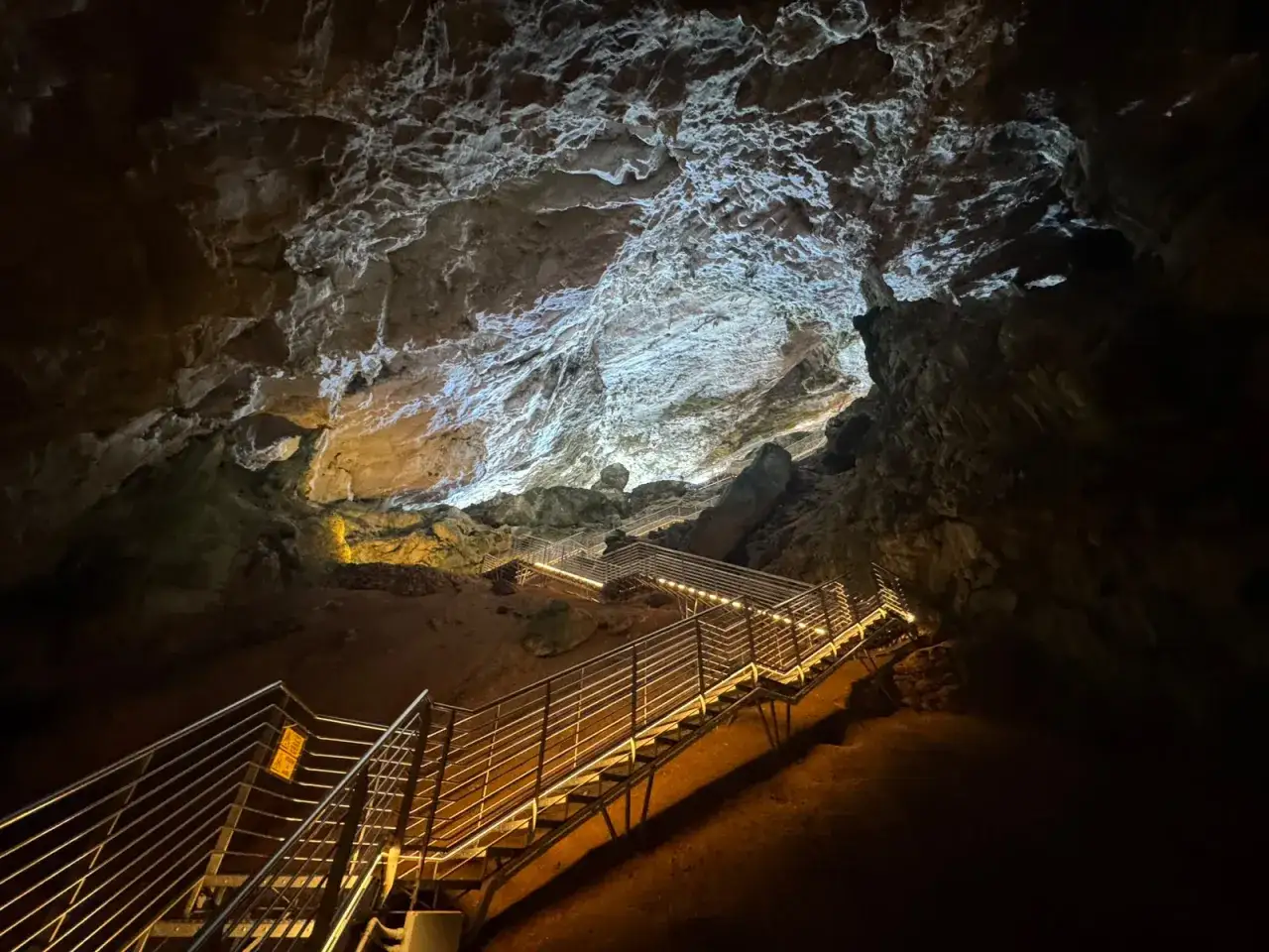 Una scalinata illuminata sale verso l'alto in una grotta verde, con rocce scolpite dalla natura e luci soffuse che creano un'atmosfera magica.