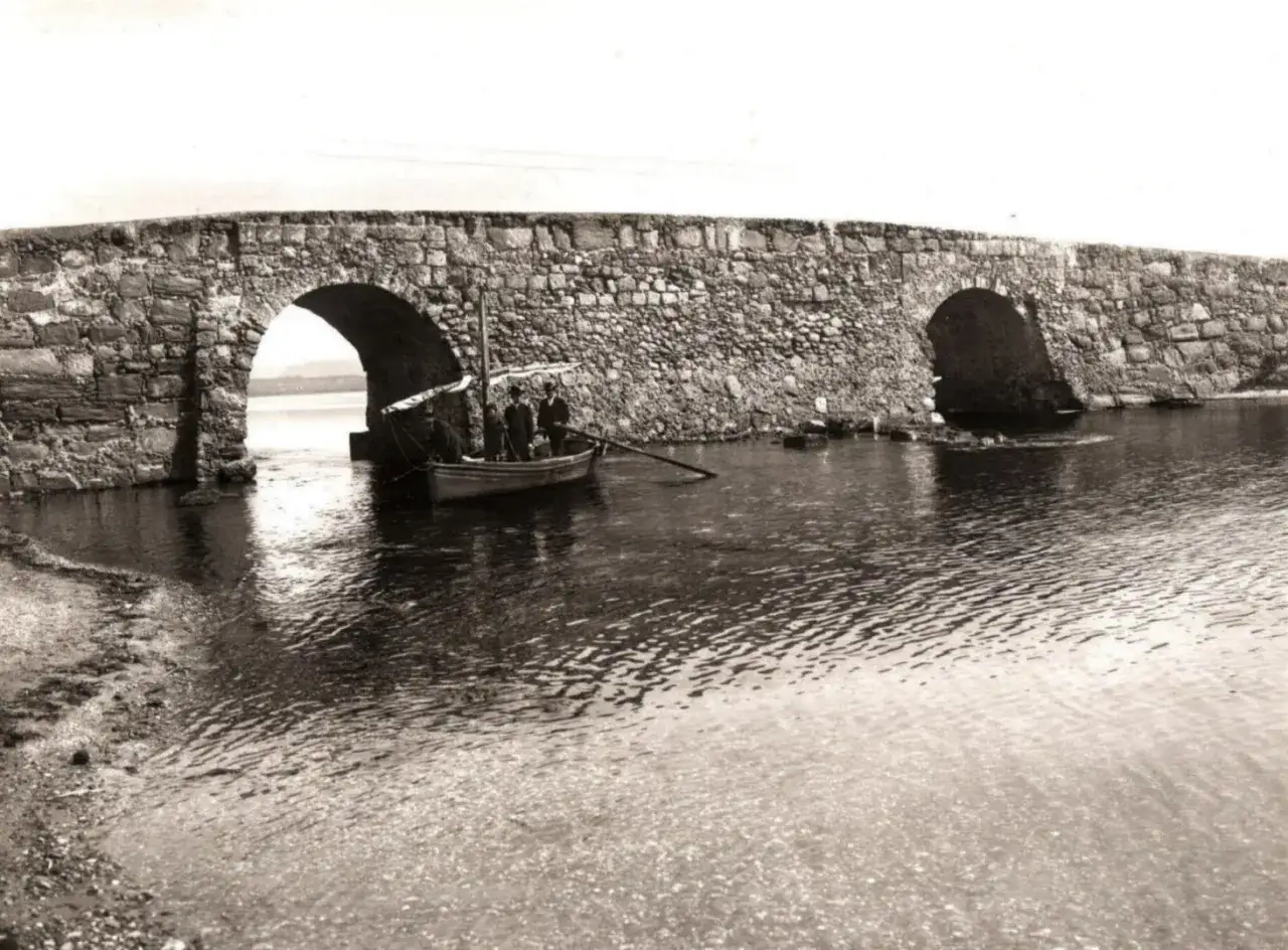 Antico ponte romano a Sant'Antioco con barca a remi e pescatori sotto un arco.