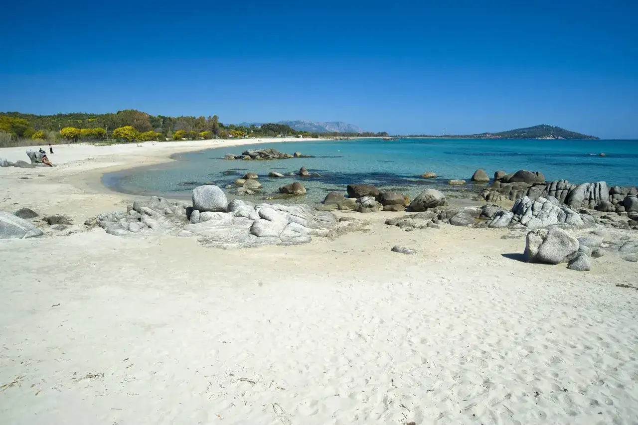 Spiaggia di Lido di Orrì con sabbia bianca, rocce levigate e mare cristallino sotto un cielo azzurro.