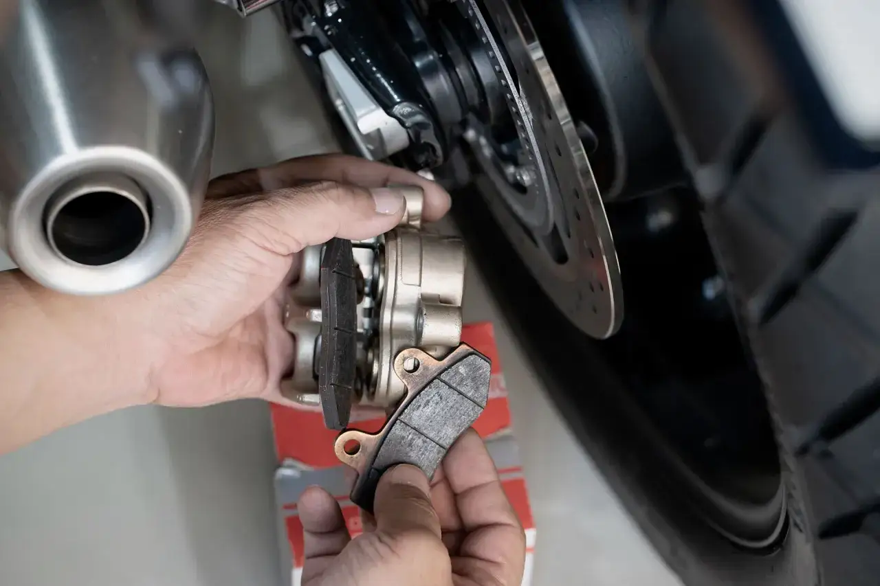 Mani che sostituiscono pastiglie freno moto usurate. Le vecchie pastiglie cristallizzate sono pronte per essere rimosse.