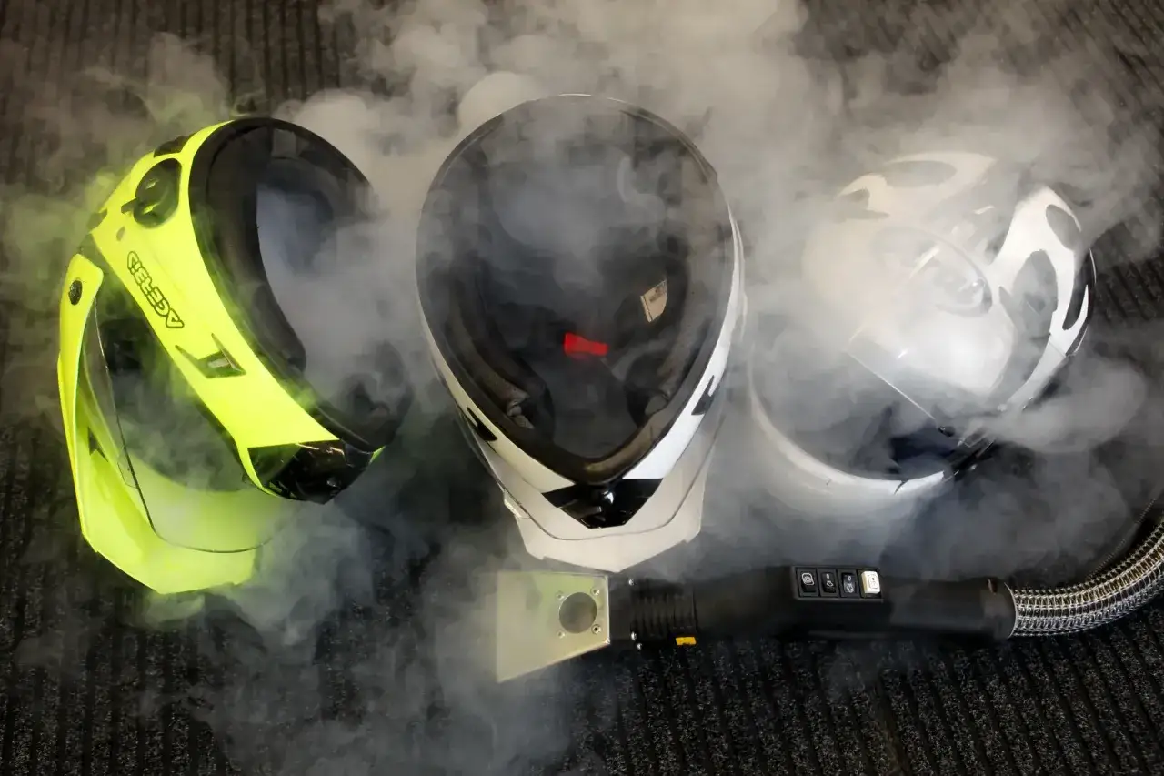 Tre caschi da moto circondati da vapore. Un accessorio per la pulizia a vapore è posizionato davanti ai caschi, suggerendo che il casco non deve essere pulito con solventi.