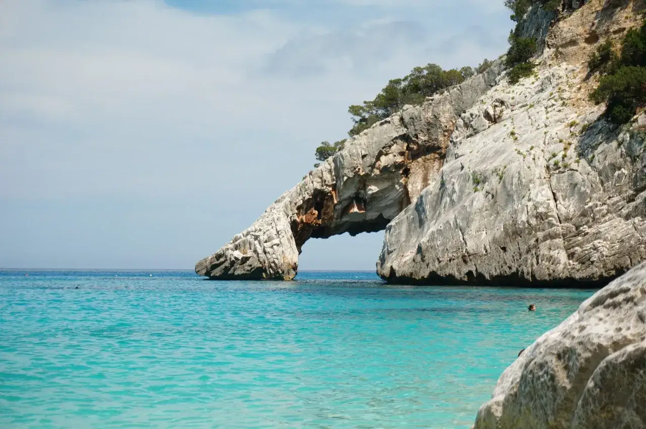 Arco naturale di roccia a Cala Goloritzé, con acque cristalline e vegetazione sulla scogliera.