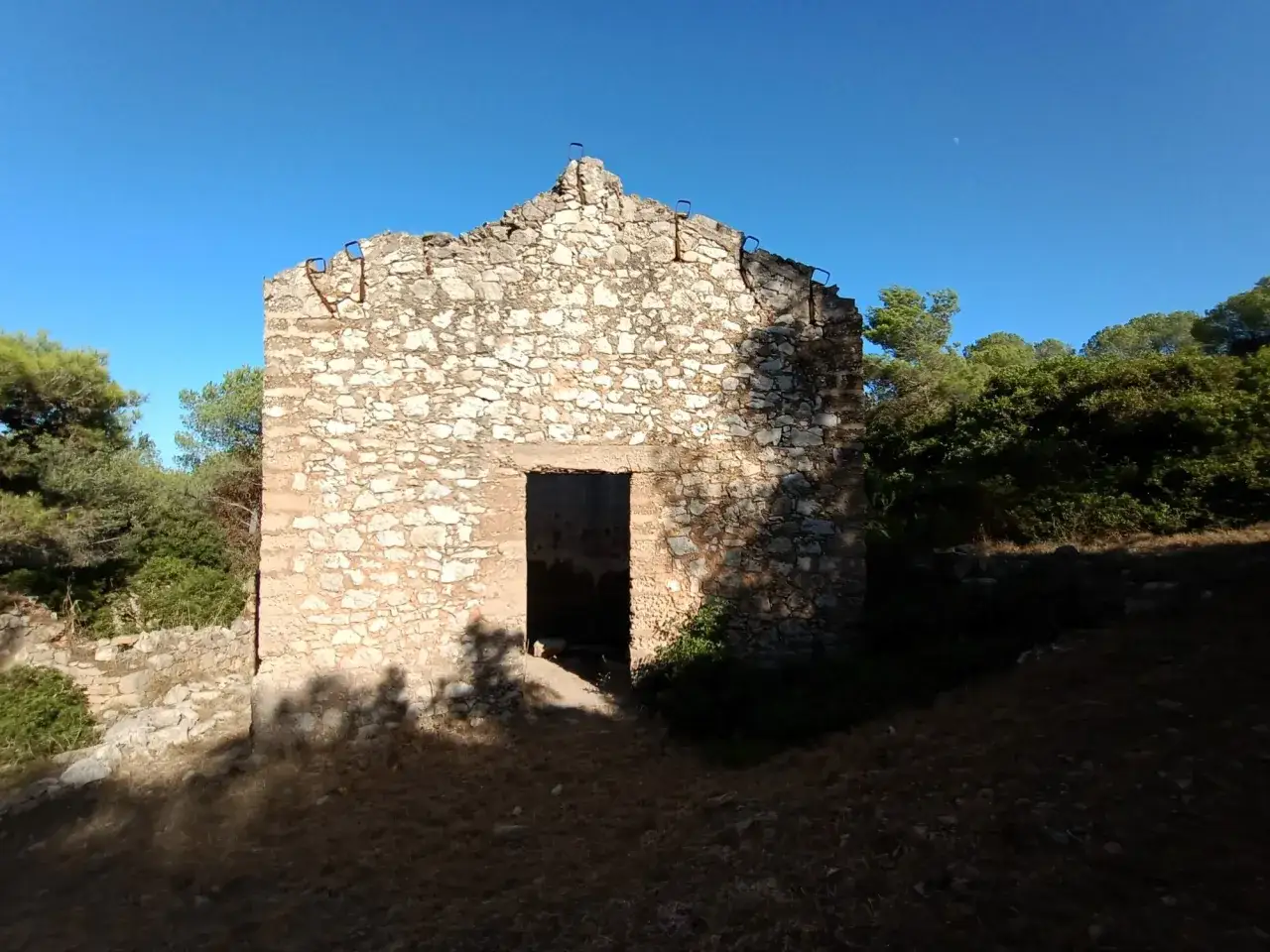 Rovine di una casa in pietra sul monte Doglia, con vegetazione circostante e cielo azzurro.