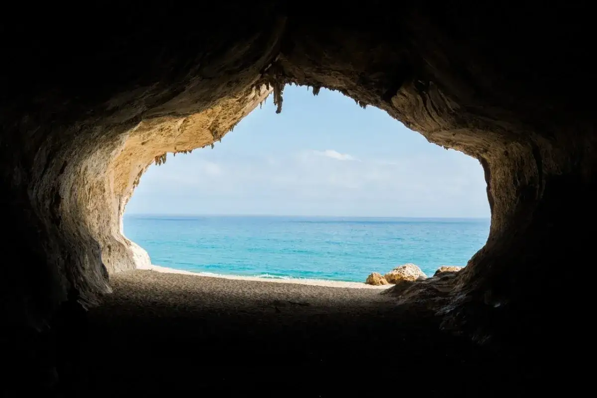 Vista dal buio di una grotta verso il mare azzurro e la spiaggia sabbiosa, un paesaggio tipico del nuorese.