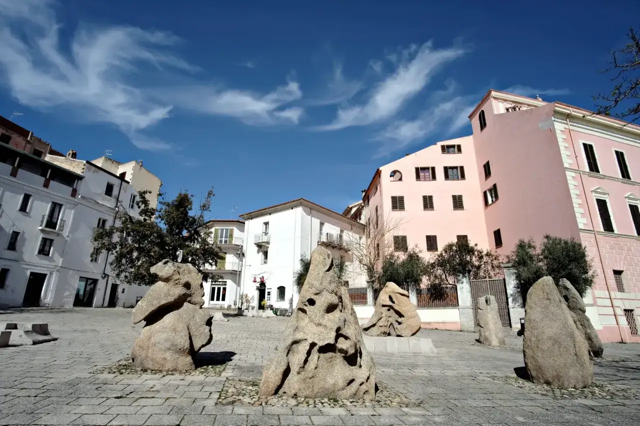 Sculture in pietra nel centro storico di Nuoro, cosa vedere: un'installazione artistica in piazza con palazzi colorati sullo sfondo.