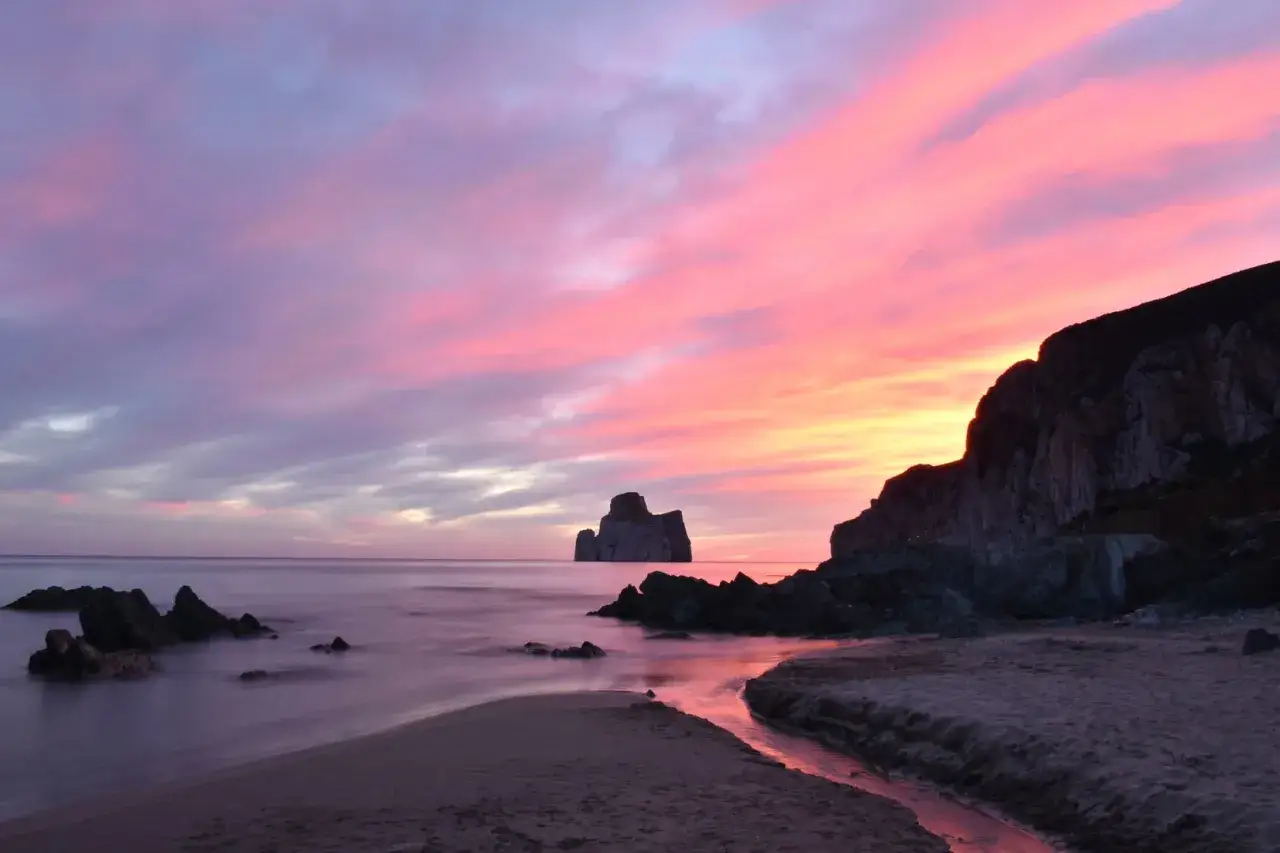 Tramonto rosa e viola sulla costa sarda, con il Pan di Zucchero che emerge maestoso dal mare.