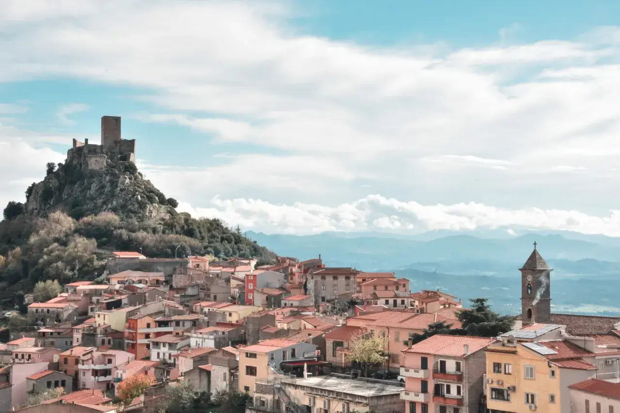 Borgo medievale di Burgos, Sardegna, con castello in rovina su una collina rocciosa e case colorate.