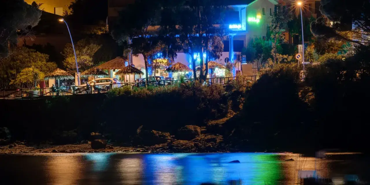Cala Gonone cosa fare la sera: un bar con tavoli all'aperto e luci blu, riflessi sull'acqua.