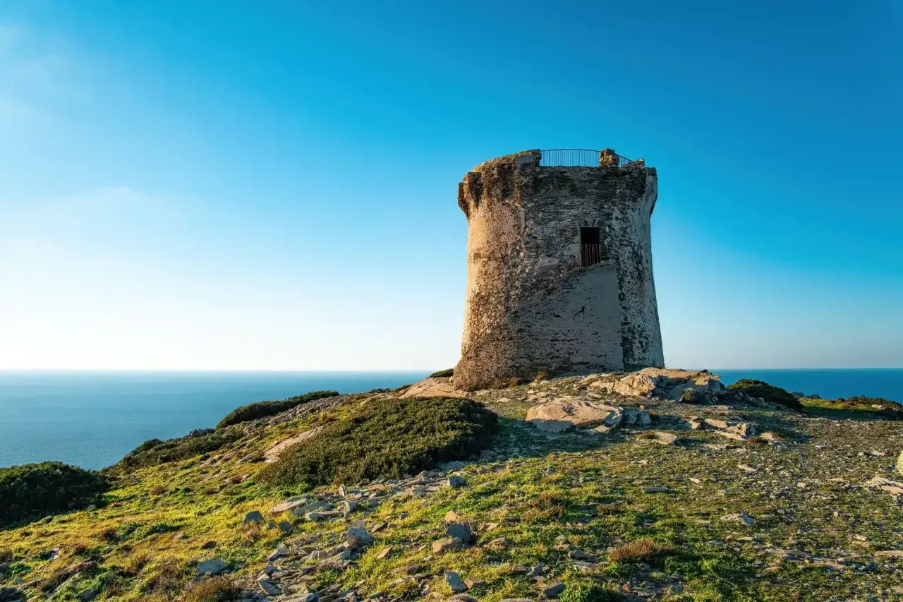 Torre costiera su un promontorio erboso, con il mare blu sullo sfondo. Un punto panoramico per capire come arrivare a Stintino.
