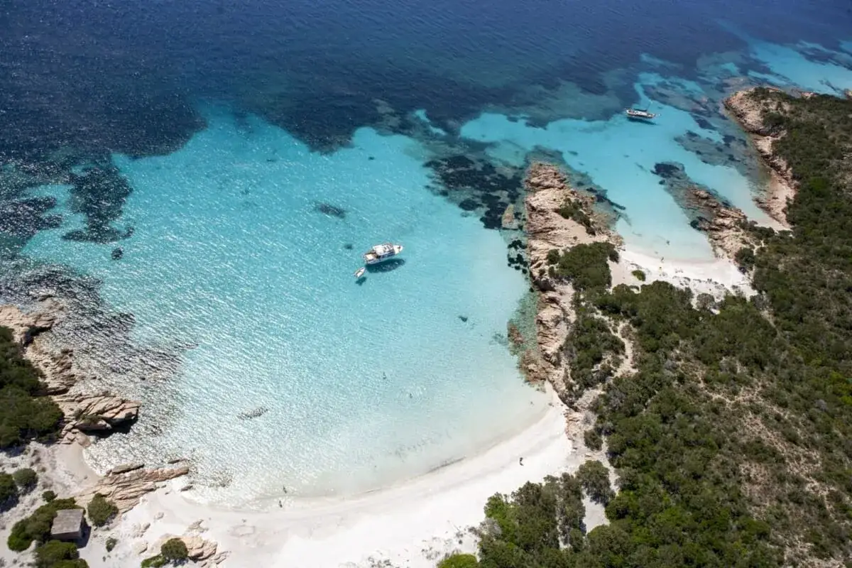 Vista aerea di Cala Granara, con acque cristalline, sabbia bianca, rocce e vegetazione mediterranea. Una barca a vela ormeggiata.