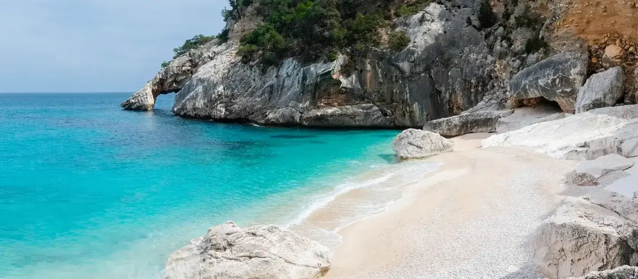 Spiaggia bianca e mare turchese vicino a Sassari, con rocce scolpite dal vento e vegetazione mediterranea.