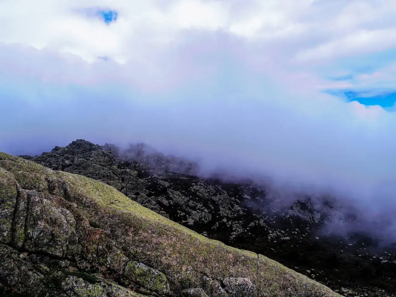 Nebbia avvolge le rocce scure di Punta Balistreri, mentre il cielo si apre in squarci azzurri.