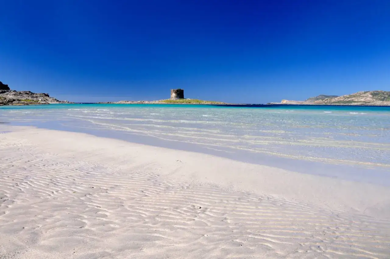 Torre aragonese su isolotto nel mare della Sardegna, con sabbia bianca e acqua cristallina.