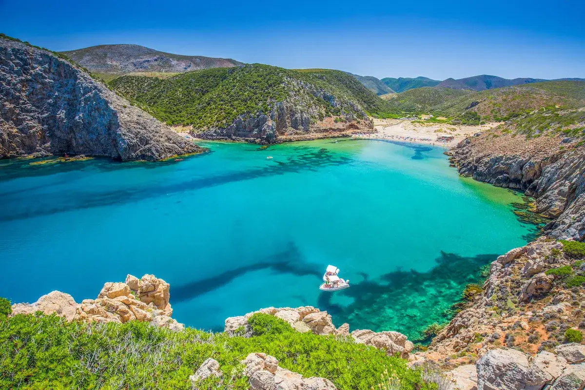 La splendida Buggerru spiaggia incanta con acque turchesi e rocce scoscese. Una barca solca il mare cristallino, mentre la sabbia dorata invita al relax.