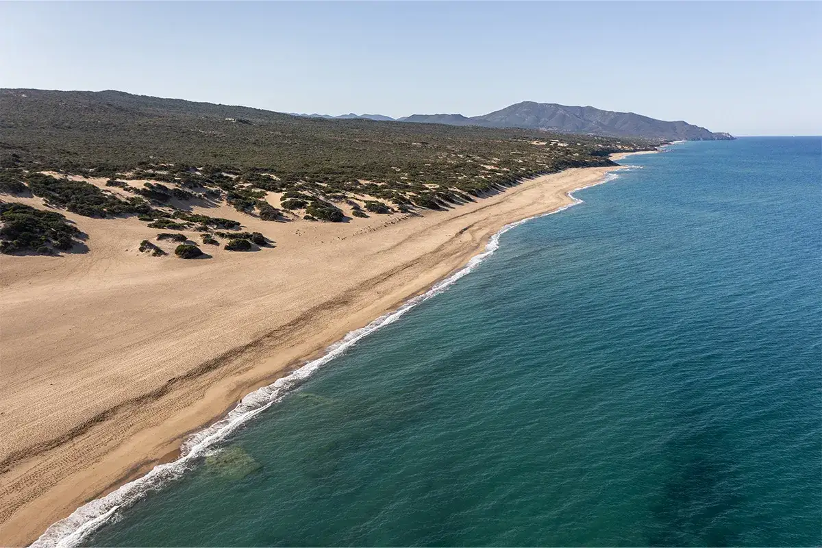 Vasta spiaggia di sabbia dorata e dune selvagge si estendono lungo la costa della spiaggia di Piscinas, bagnata da un mare cristallino.