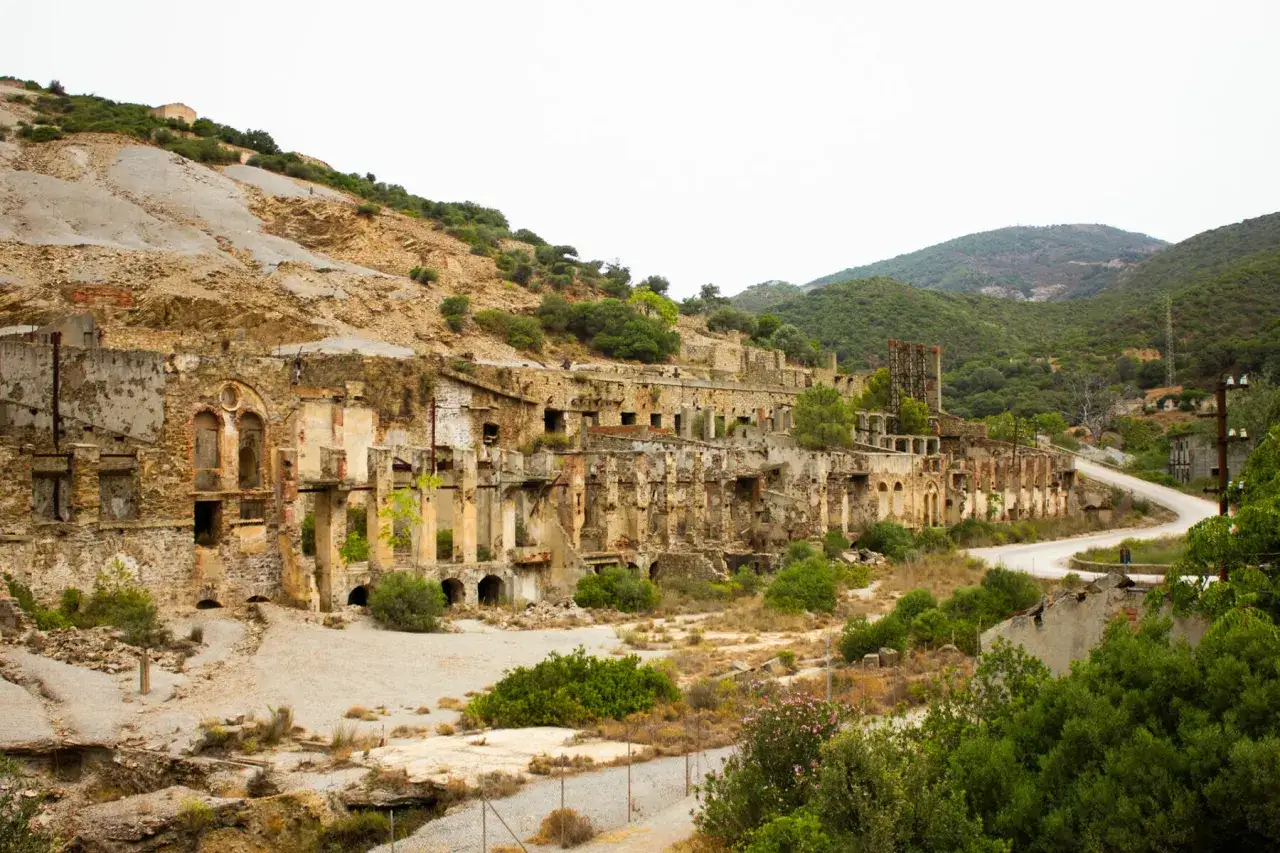 Rovine di antiche miniere abbandonate in Sardegna, con edifici in rovina e vegetazione che si riappropria del paesaggio.