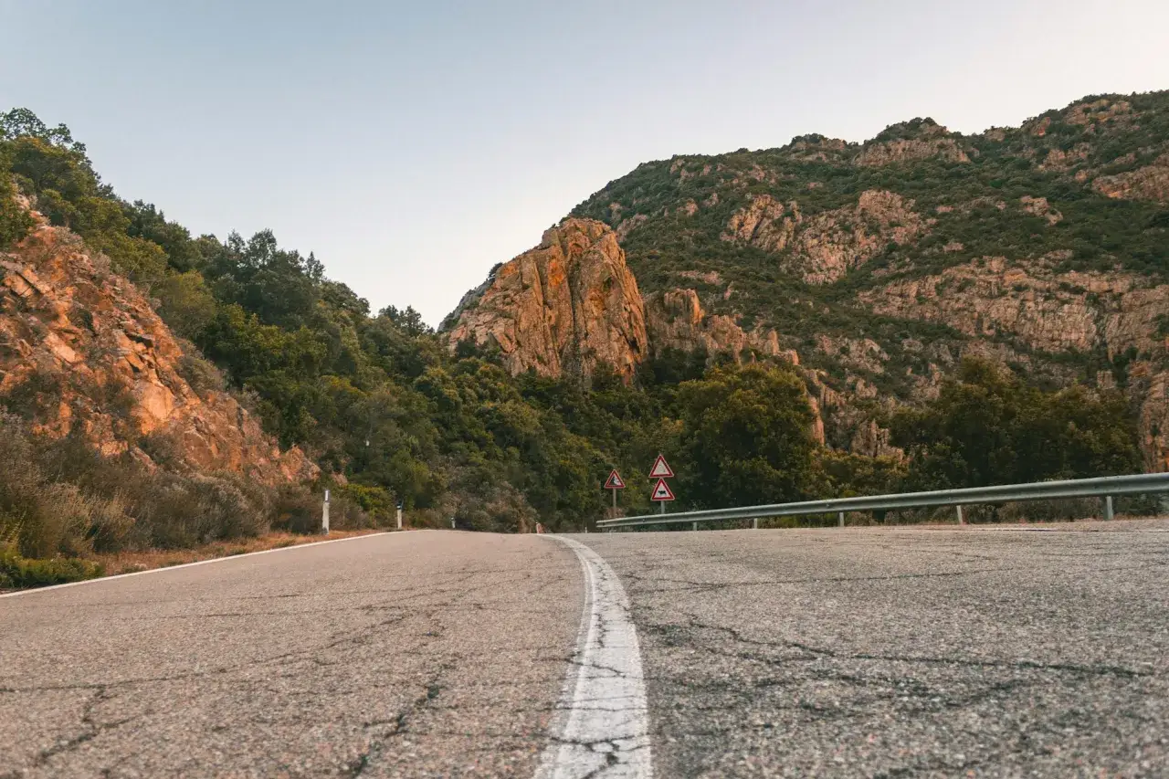 Strada panoramica verso Chia, Cagliari, tra montagne rocciose e vegetazione rigogliosa.