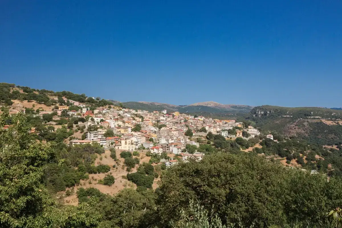 Panoramica di Seulo, Sardegna, con case colorate arroccate su una collina verdeggiante sotto un cielo azzurro.
